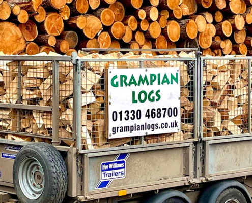 Grampian Logs trailer loaded with firewood in front of stacked timber