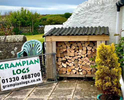 Neatly stacked firewood in a garden log store beside a Grampian Logs sign